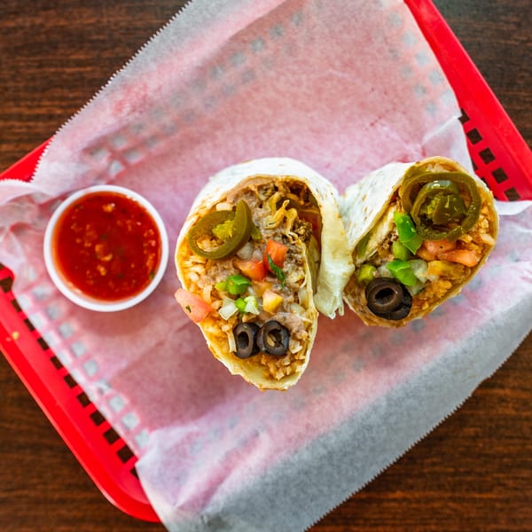 Two Uno Dos Tacos burritos, cut in half, filled with meat, rice, beans, and vegetables, with a side of salsa.
