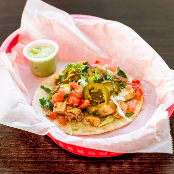 A chicken taco with lettuce, tomatoes, onions, cilantro, and jalapeños, served with green salsa.