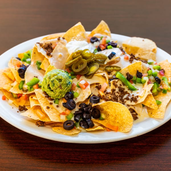 A plate of Uno Dos Tacos nachos with cheese, ground beef, guacamole, sour cream, jalapeños, and olives.